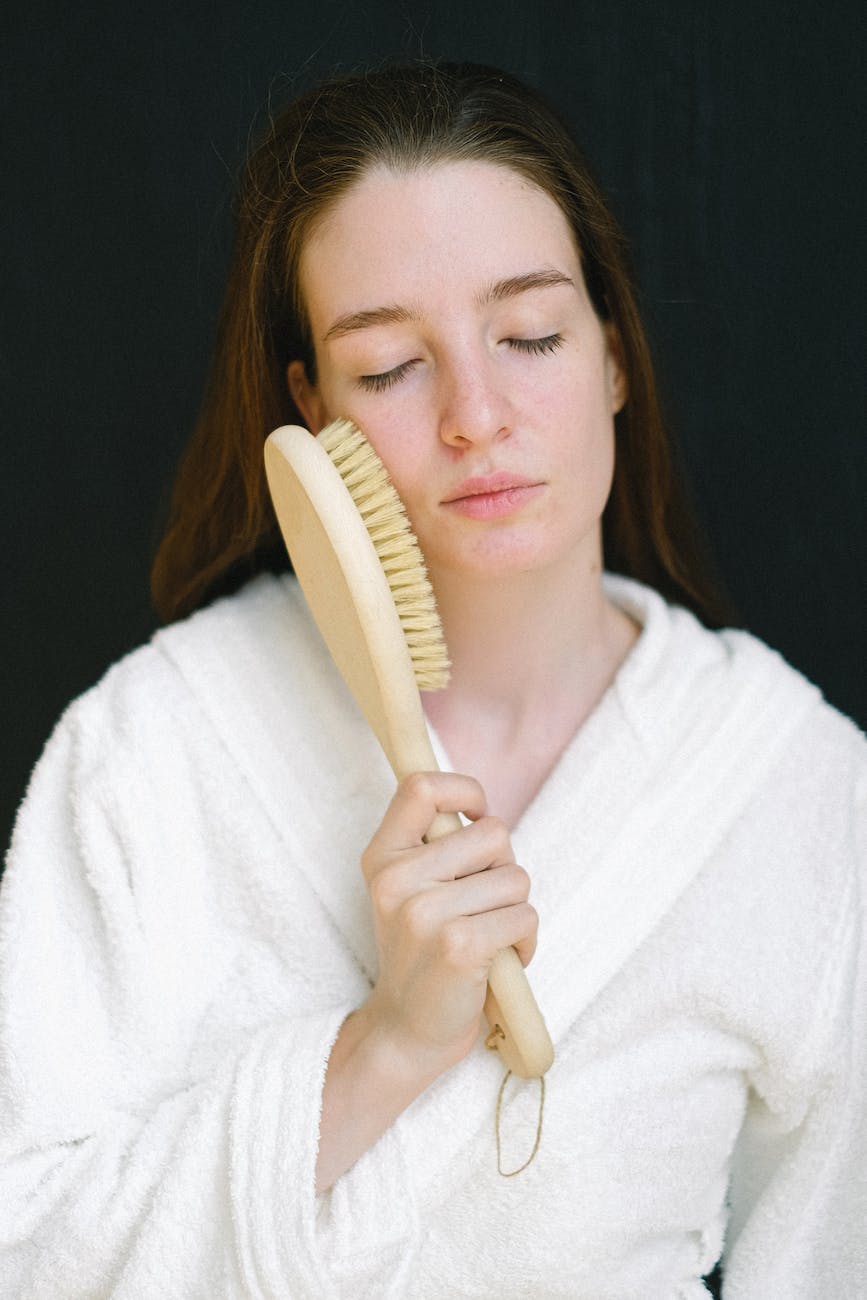 tranquil model in bathrobe doing facial massage with natural bamboo hair brush