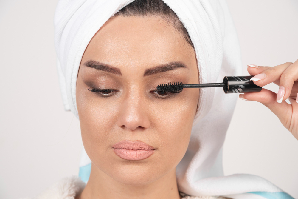 woman in white towel applying mascara