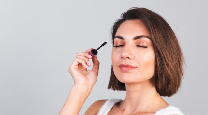 The Complete Guide to Mascara: Transform Your Lashes for Every Occasion Beautiful woman with makeup hold black mascara brush on gray wall